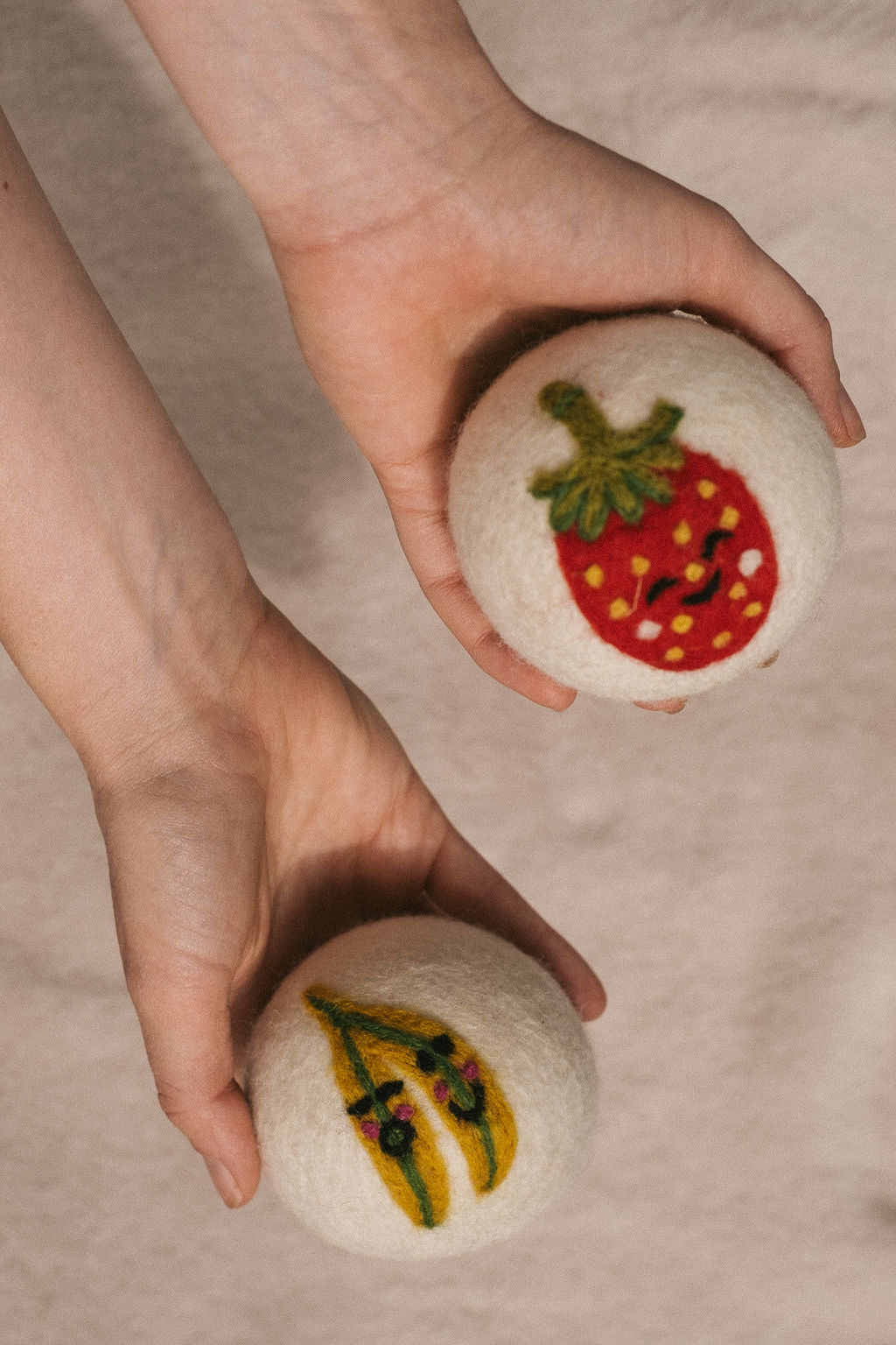 Hands holding the Strawberry and Two Bananas dryer balls